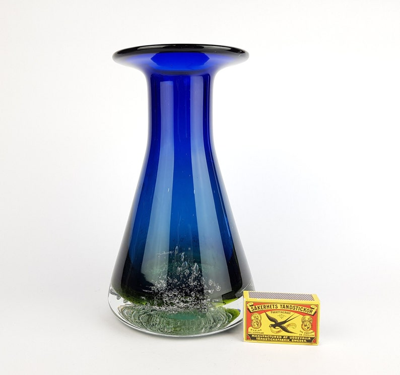 May include: A cobalt blue glass vase with a wide mouth and a rounded base. The vase has a textured, white and green design at the bottom.