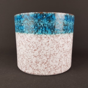 May include: A white ceramic planter with a blue and brown speckled glaze. The planter has a wide, round opening and a slightly tapered base.