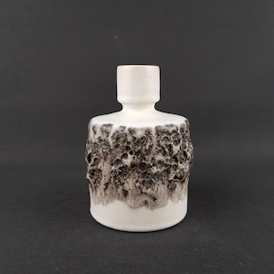 Peut inclure: Un vase en céramique blanc avec une partie inférieure texturée, gris foncé et marron. Le vase a une forme cylindrique avec un col étroit et cylindrique. La surface a une texture rugueuse et organique.