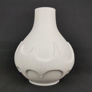May include: White ceramic vase with a textured, ribbed surface and a unique, geometric design. The vase has a rounded, bulbous shape with a narrow neck.