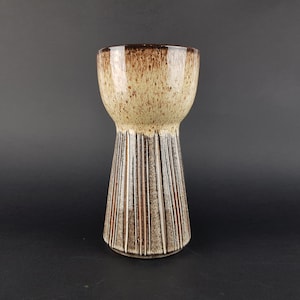 May include: A ceramic vase with a brown and white speckled glaze. The vase has a wide mouth and a narrow base, with vertical lines around the middle.