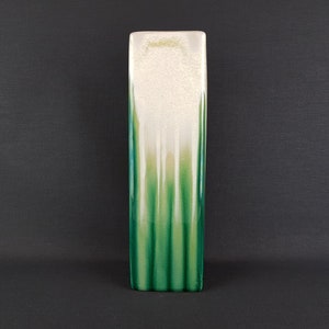 Peut inclure: Un vase en céramique rectangulaire et haut, avec un dessus blanc et un fond vert. Le glaçage vert a un motif strié.