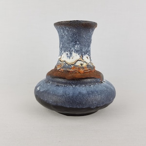 May include: A ceramic vase with a bulbous base and a flared top. The vase features a textured, mottled blue glaze with brown and white accents around the middle. The base is dark, and the overall design is rustic.