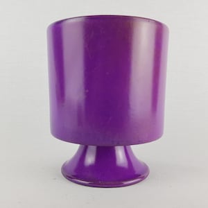 Puede incluir: Un jarrón de cerámica morado con un cuerpo cilíndrico ancho y una base acampanada.