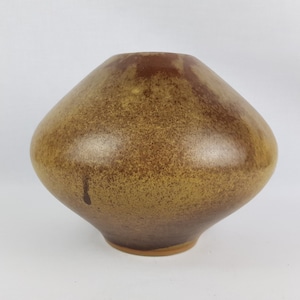 May include: A brown ceramic vase with a speckled glaze. The vase has a wide, rounded base and a narrow opening.
