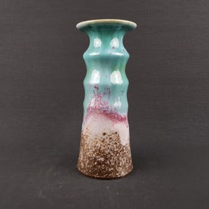 Puede incluir: Una taza de cerámica blanca con un asa negra y el texto "But First, Coffee" en negrita negra. La taza se encuentra sobre un fondo borroso, sugiriendo un ambiente acogedor.