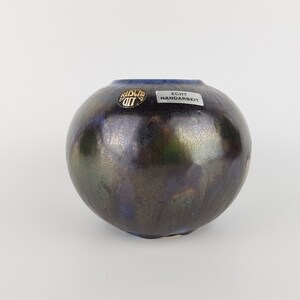 May include: A small, round, black and blue ceramic vase with a gold sticker that says "ECHT HANDARBEIT".