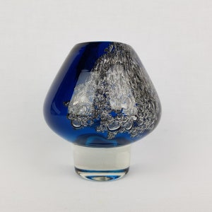 Puede incluir: Un jarr&oacute;n de vidrio azul con un dise&ntilde;o de remolino blanco y plateado. El jarr&oacute;n tiene una base ancha y redondeada y un cuello estrecho.