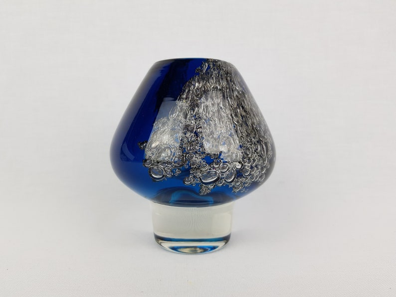 Puede incluir: Un jarr&oacute;n de vidrio azul con un dise&ntilde;o de remolino blanco y plateado. El jarr&oacute;n tiene una base ancha y redondeada y un cuello estrecho.