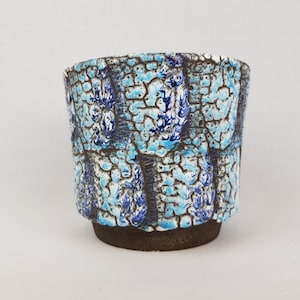 May include: A blue and white ceramic planter with a crackled glaze. The planter has a brown base and a cylindrical shape.