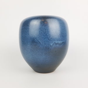 Puede incluir: Un jarrón de cerámica redondeado con un esmalte azul profundo y una textura moteada. El recipiente tiene una silueta suave y curva que se estrecha hacia una base angosta, mostrando un degradado de tonos azul marino a azul cobalto.