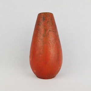 Puede incluir: Un jarrón de cerámica de color terracota con forma de lágrima. El jarrón tiene un esmalte moteado y desigual.