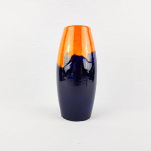 Puede incluir: Un jarrón alto de cerámica con acabado brillante. La mitad superior es de color naranja brillante, que pasa a un azul marino intenso en la parte inferior. El jarrón tiene una forma suave y redondeada, adecuado para flores o como elemento decorativo.