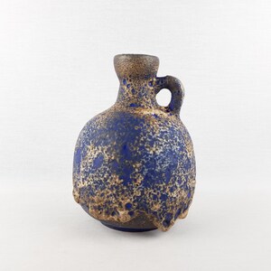 May include: A blue and brown ceramic vase with a handle. The vase has a textured surface with a speckled pattern. The vase has a round body and a small opening at the top.
