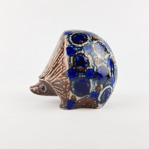May include: A ceramic hedgehog ornament with a brown body and a spiky back. The back is decorated with blue and white circular patterns. The hedgehog has a small, pointed snout and tiny blue eyes. A decorative item.