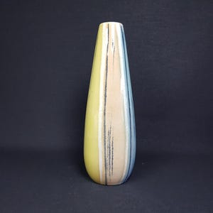 Op de afbeelding: Een hoge, slanke keramische vaas met een geel, beige en blauw gestreept ontwerp. De vaas heeft een gladde, glanzende afwerking.