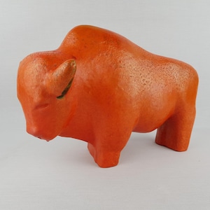 Puede incluir: Escultura de cerámica naranja de un bisonte. La escultura es estilizada y tiene una superficie texturizada.