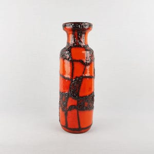 Könnte beinhalten: Eine hohe, orangefarbene und braune Keramikvase mit einem strukturierten, geometrischen Design. Die Vase hat einen schmalen Hals und einen breiten Boden. Die orangefarbenen Abschnitte sind glänzend, während die braunen Abschnitte eine raue, matte Oberfläche haben. Die Vase ist etwa 25 cm hoch.