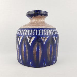 May include: A ceramic vase with a rounded body and a narrow neck. The vase features a blue and brown geometric pattern on a cream-colored background. The vase is approximately 8 inches tall.