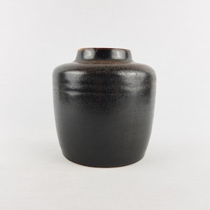May include: A dark brown ceramic vase with a speckled, textured surface. The vase has a rounded body and a slightly flared rim. The interior rim is a lighter brown color.