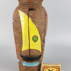 Puede incluir: Un jarr&oacute;n de cer&aacute;mica marr&oacute;n con un dise&ntilde;o de velero amarillo, verde y azul. El jarr&oacute;n tiene una superficie texturizada y mide aproximadamente 30 cm de alto.