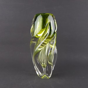 Può includere: Un vaso di vetro trasparente con un design a spirale verde e bianco. Il vaso ha una forma arrotondata e una parte superiore svasata. I colori verde e bianco creano un contrasto sorprendente. Il vaso è alto circa 25 cm.