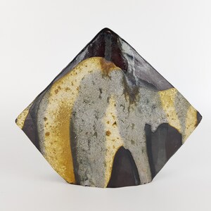 Puede incluir: Un jarrón de cerámica con un diseño geométrico en forma de diamante. El jarrón está esmaltado en tonos de marrón, negro, gris y amarillo.