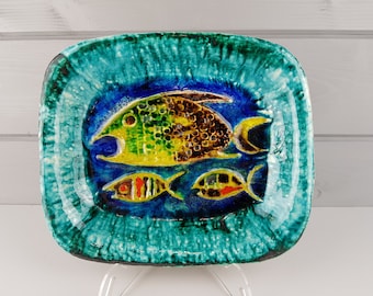 May include: A rectangular ceramic dish with a glossy finish, featuring a deep blue center decorated with one large yellow and brown fish above two smaller fish with red, yellow, and black accents, all framed by a textured, vibrant teal border.