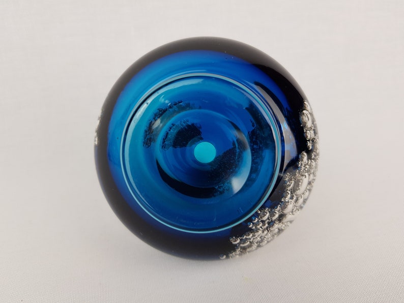 Puede incluir: Un pisapapeles de vidrio azul con un dise&ntilde;o plateado de burbujas en el lateral. El pisapapeles tiene un centro transparente con un anillo azul alrededor.