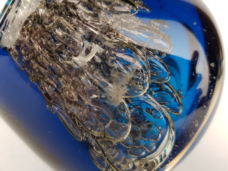 Puede incluir: Primer plano de un pisapapeles de vidrio azul con un dise&ntilde;o claro y texturizado en su interior. El vidrio es transparente y tiene una superficie lisa y brillante.