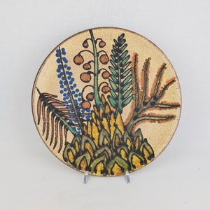 May include: A ceramic plate with a hand-painted design of stylized flowers in shades of brown, green, blue, and yellow.