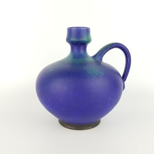 Peut inclure: Un vase en céramique bleu et vert avec un corps arrondi et une seule anse. Le vase a un glaçage texturé.