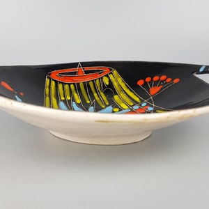 May include: A ceramic serving dish with a black interior and a white exterior. The dish features a colorful abstract design with yellow, red, and blue accents. It has handles with blue stripes and measures approximately 12 inches in length.