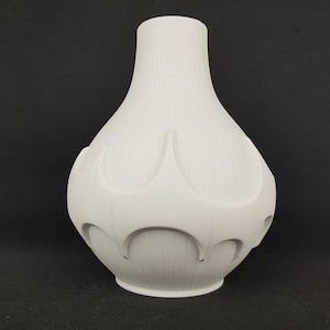 May include: White ceramic vase with a unique, abstract design. The vase has a rounded, bulbous shape with a narrow neck and a textured, ribbed surface.