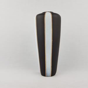 May include: A tall, cylindrical vase with a matte black finish, featuring vertical stripes of pale blue glaze separated by thin, raised gold-toned lines that run from the top rim down to the base of the vessel, creating a structured appearance.