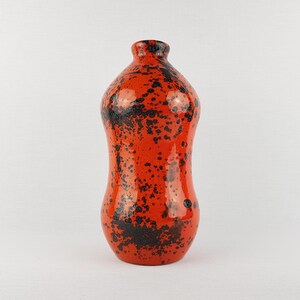 May include: A tall, ceramic vase with a rounded body and narrow neck. The vase is a vibrant orange color, speckled with black spots. The glossy finish adds to its decorative appeal. A unique piece for home decor.