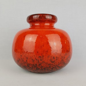 Puede incluir: Un jarrón redondo de cerámica naranja con un esmalte marrón oscuro en la parte inferior. El jarrón tiene un acabado brillante.