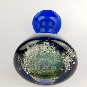 May include: A blue glass vase with a green and white bubble design. The vase has a wide mouth and a narrow base.