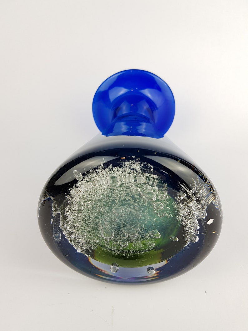 May include: A blue glass vase with a green and white bubble design. The vase has a wide mouth and a narrow base.