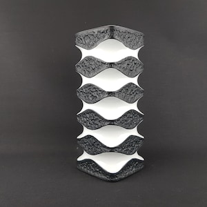 May include: A black and white ceramic vase with a geometric design. The vase is made up of stacked, wavy, black and white sections.