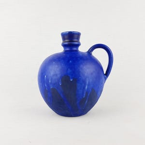 Peut inclure: Pichet en céramique bleu cobalt avec un corps arrondi et une petite anse. Des coulures d'émail bleu foncé descendent sur le devant, créant un effet texturé. Le pichet a un petit col cylindrique.