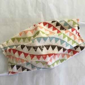 May include: A face mask made of white fabric with a colorful geometric pattern of triangles and stripes. The pattern is in shades of red, orange, pink, green, blue, and brown.