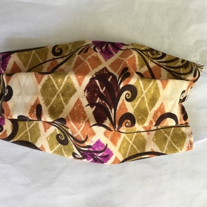 May include: A face mask with a brown, green, orange, and purple floral pattern on a white background. The mask has white elastic ear loops.