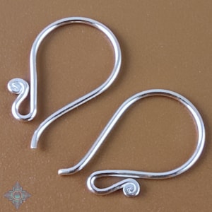 May include: Two silver-colored earring hooks. Each hook has a curved design with a looped end and a decorative swirl at the bottom. The hooks are displayed against a brown background.