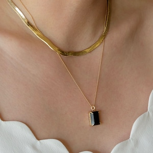 May include: A gold chain necklace with a black rectangular pendant. The necklace is layered over a second gold chain.