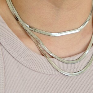 May include: A silver chain necklace with a layered design. The necklace is made of multiple thin chains that are linked together to create a layered effect.