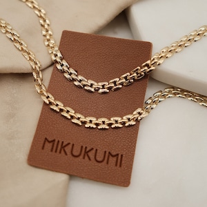 May include: Two gold chain necklaces on a brown leather tag with the word "MIKUKUMI" embossed on it. The necklaces are made of a box chain style.