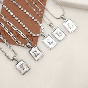 May include: Five silver necklaces with rectangular pendants featuring the letters Y, R, S, B, and L. The pendants have a white background and the letters are engraved in black.