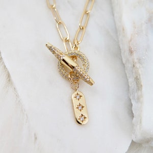 May include: Gold necklace with a toggle clasp and a small pendant with three star-shaped accents. The necklace is made of a chain link design.