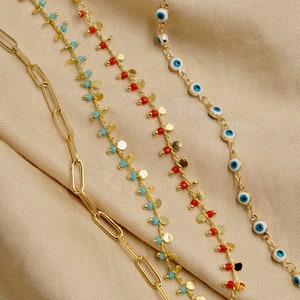 May include: Three gold chains with different charms. The first chain has small gold discs and red beads. The second chain has small gold discs and turquoise beads. The third chain has blue evil eye charms.